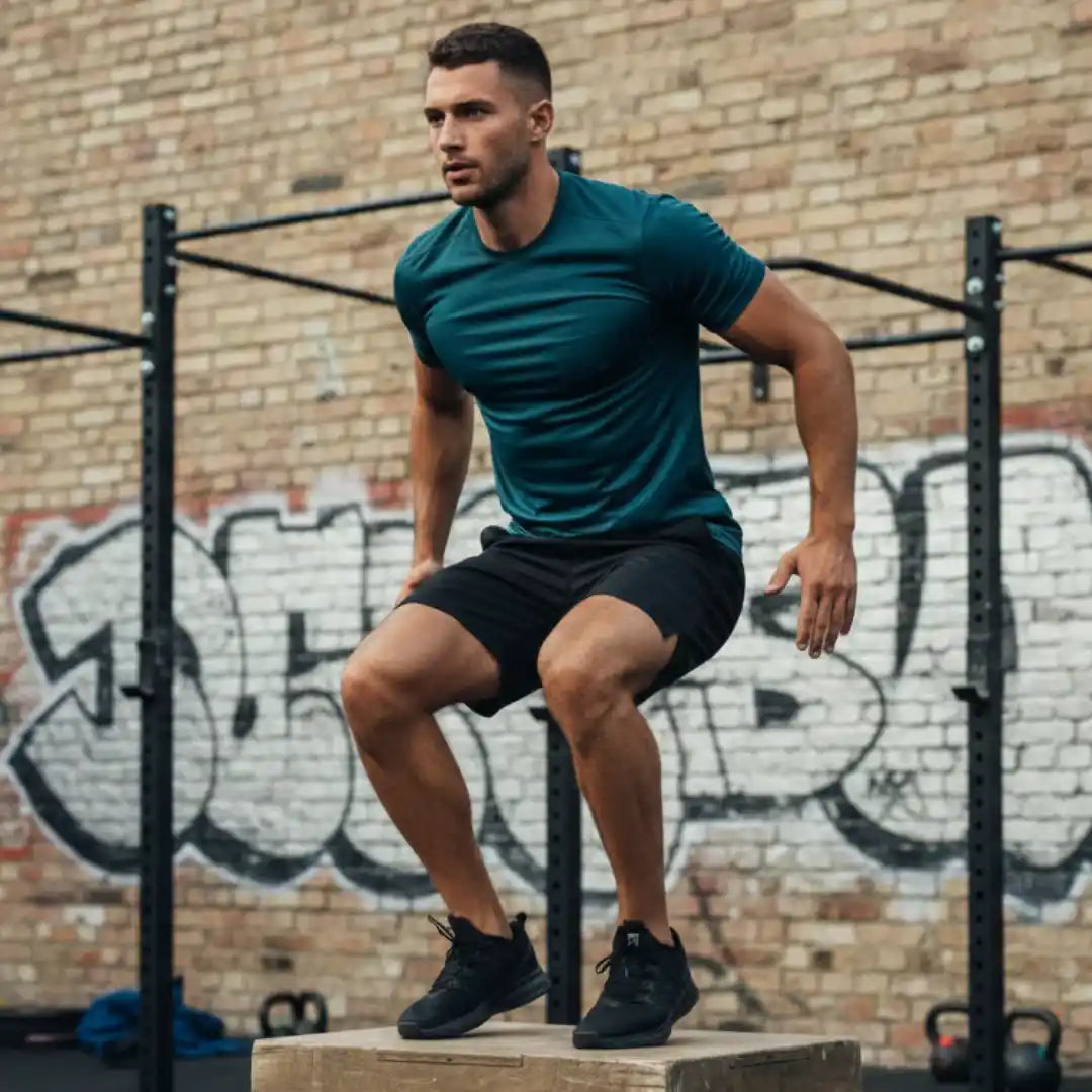 thletic man wearing Rovarix athletic apparel black mesh gym shorts performing box jumps at outdoor