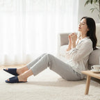 Woman wearing Rovarix navy blue indoor slippers relaxing at home in comfortable lounge setting