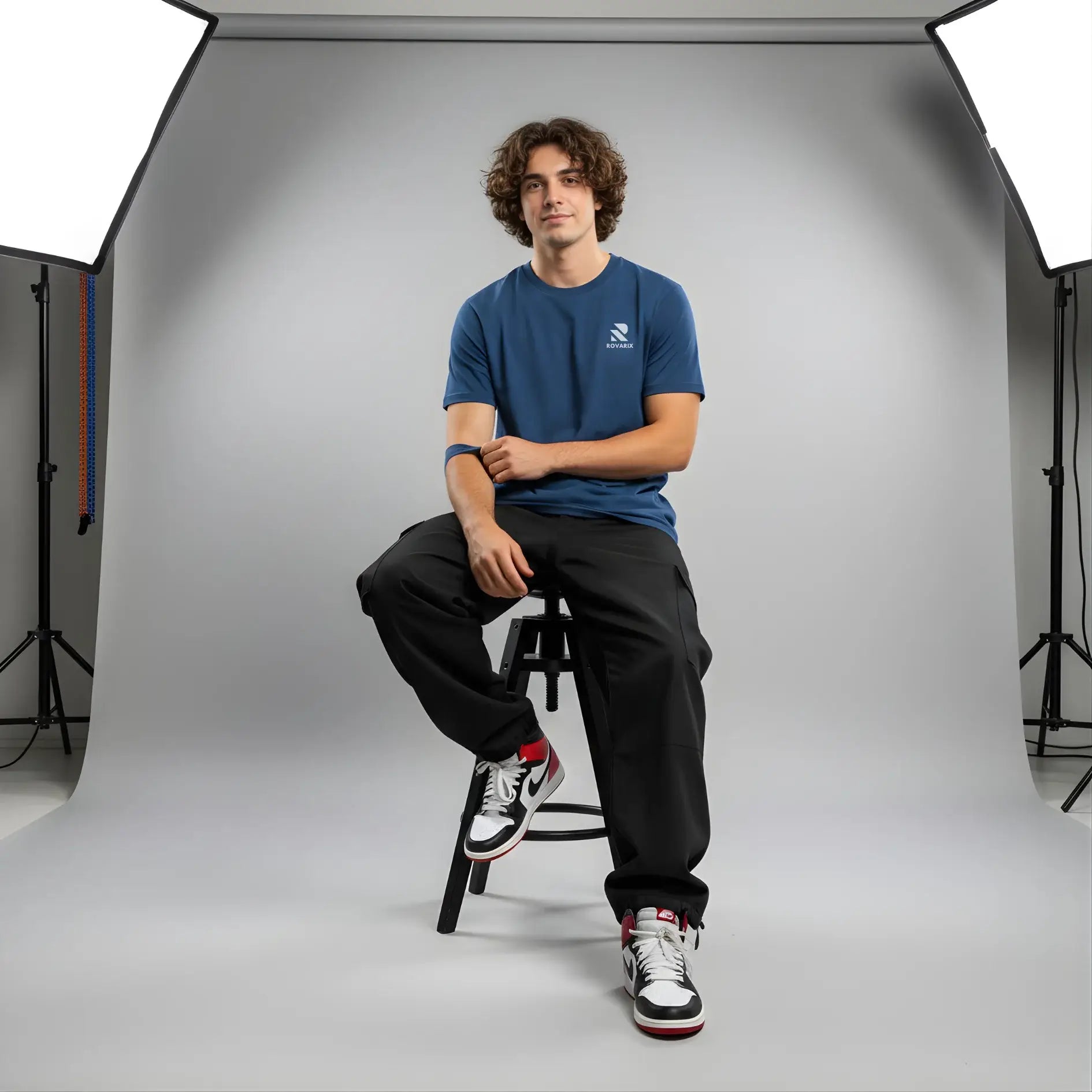 Man sitting on a stool in a studio setting with photography equipment.