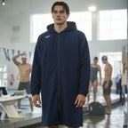 Male swimmer wearing Rovarix navy blue knee-length swim parka with hood standing on pool 