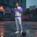 Man in a purple and gray tracksuit standing on a rain-soaked basketball court with graffiti in the background.