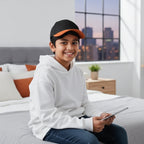 Young person wearing Rovarix black and orange two-tone baseball cap with white hoodie indoors