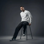 Man sitting on a stool wearing a Rovarix white sweatshirt and black pants against a dark background